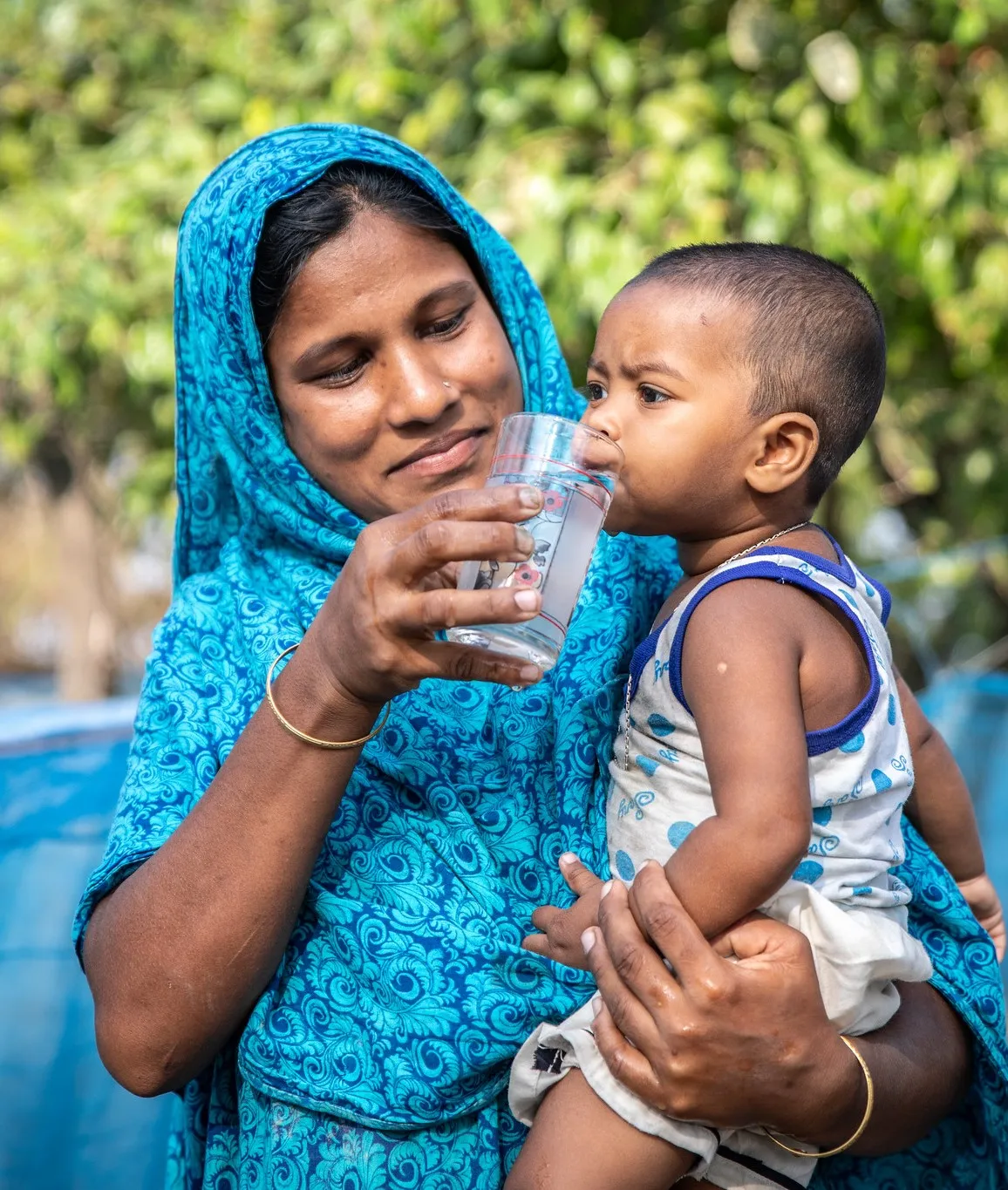 Doli holding a glass of water up to her child.