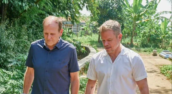 Water.org cofounders Matt Damon and Gary White walk down a path with greenery in the background.