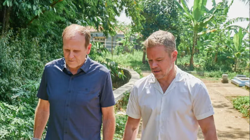 Water.org cofounders Matt Damon and Gary White walk down a path with greenery in the background.