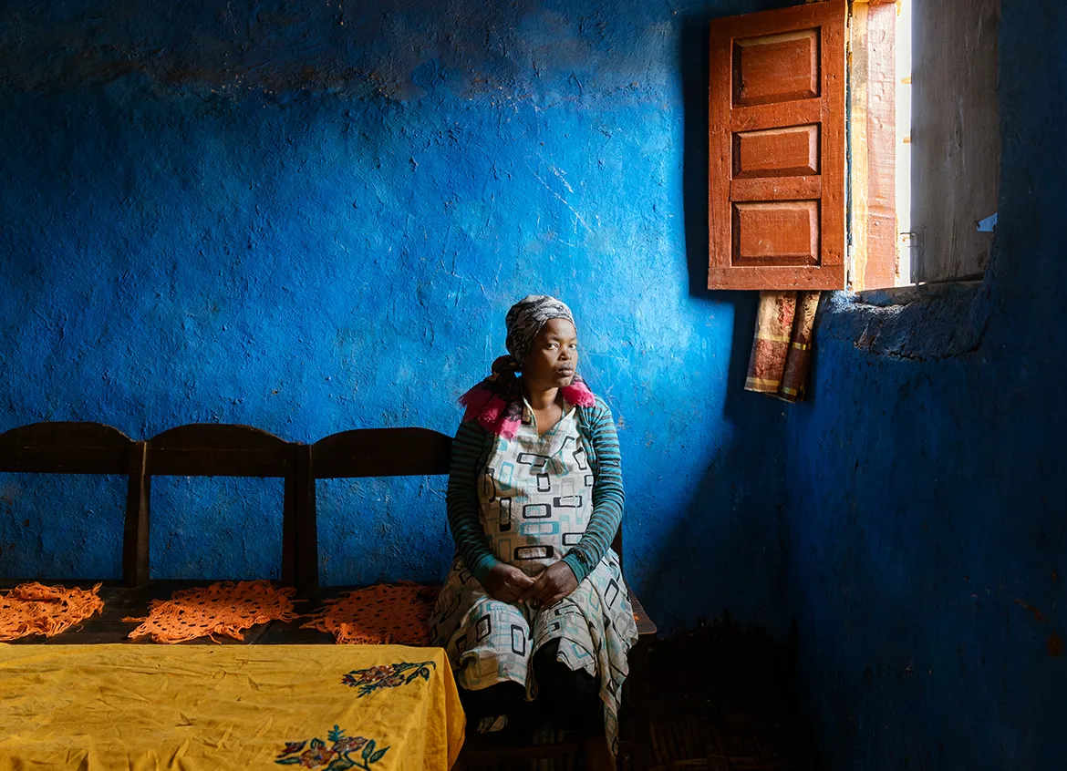 Grace, a woman in Ethiopia sitting on a chair in front of a blue wall.