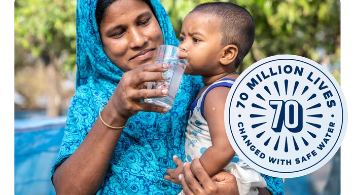 A woman in Bangladesh giving her baby a drink of water from a clear glass.