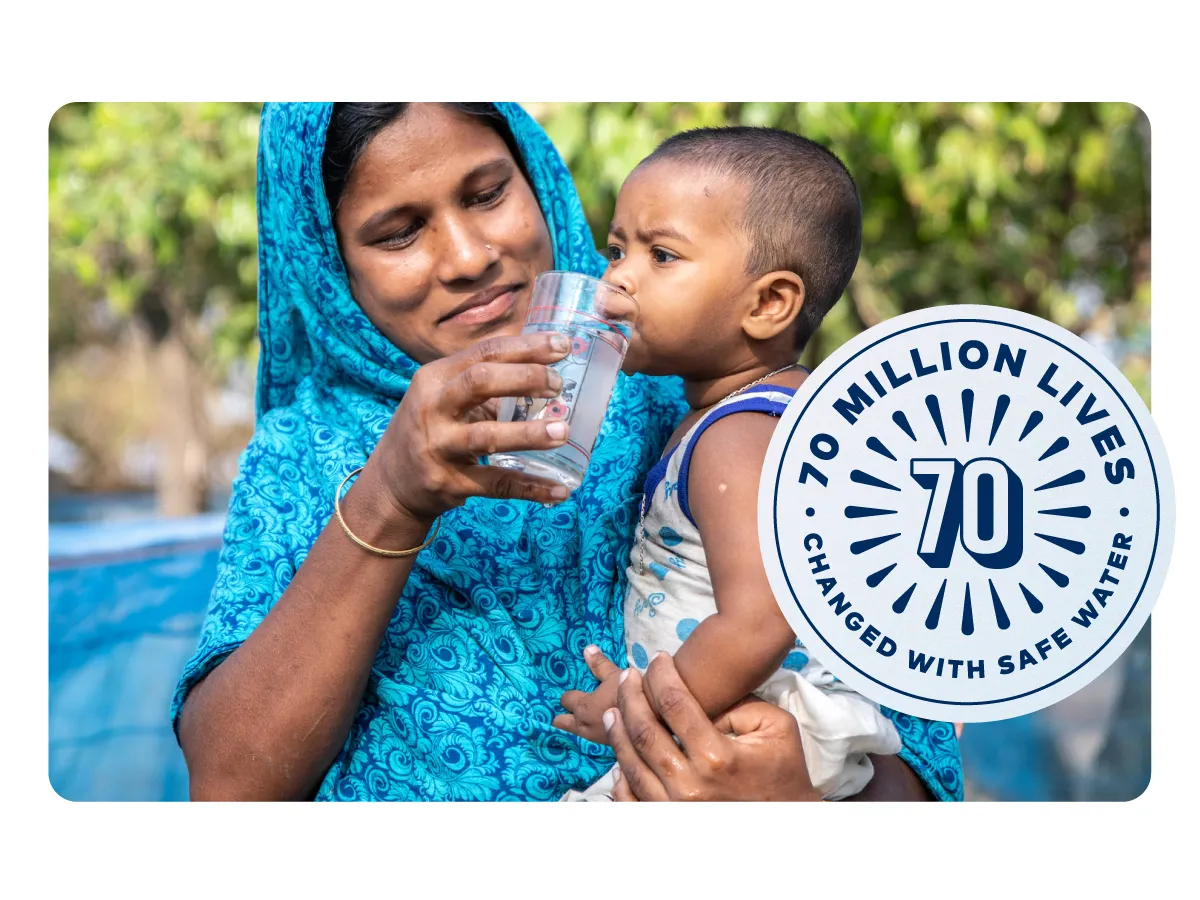 A woman in Bangladesh giving her baby a drink of water from a clear glass.