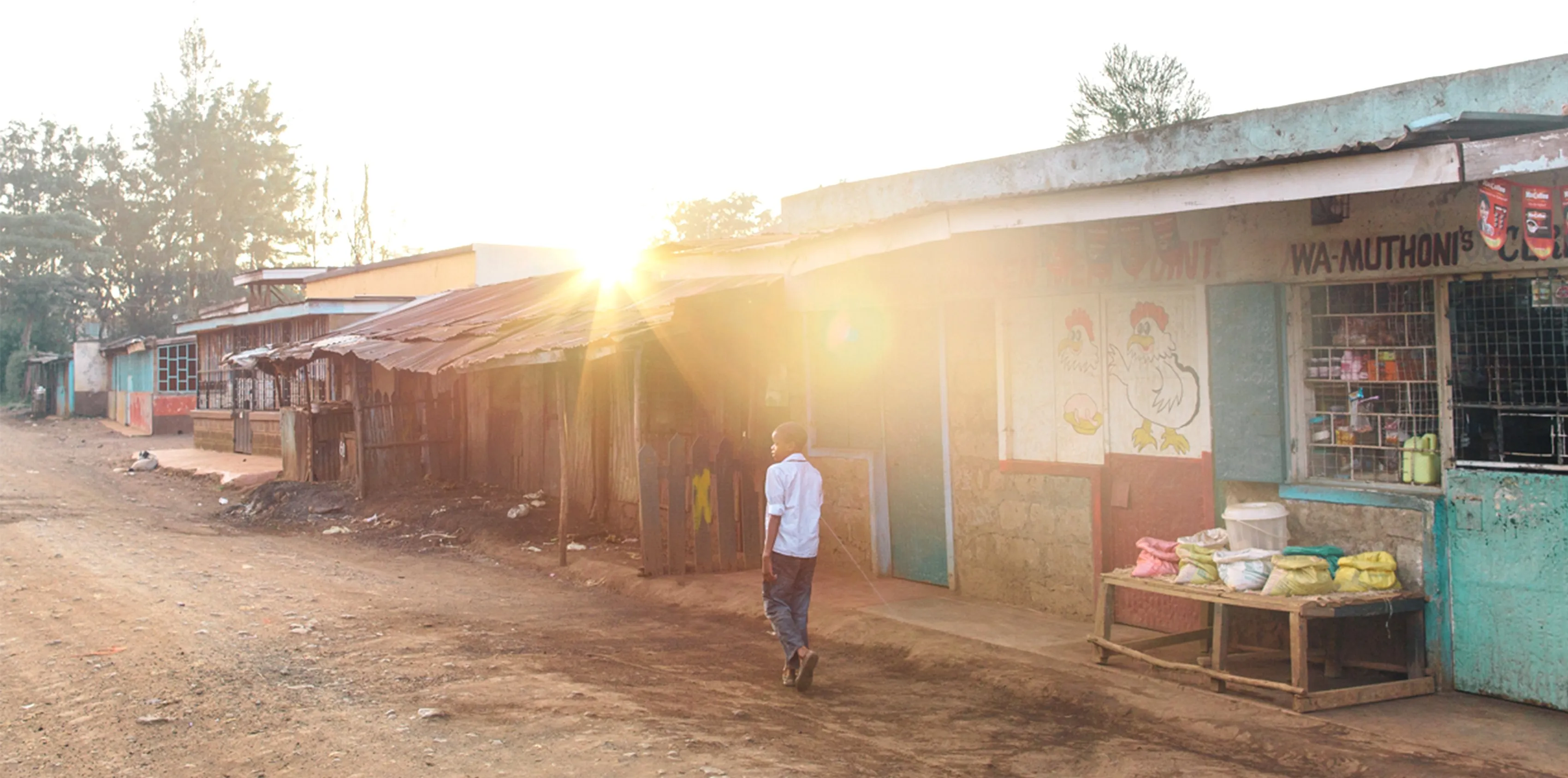 Young boy walking on the road in front of shops in Kenya.