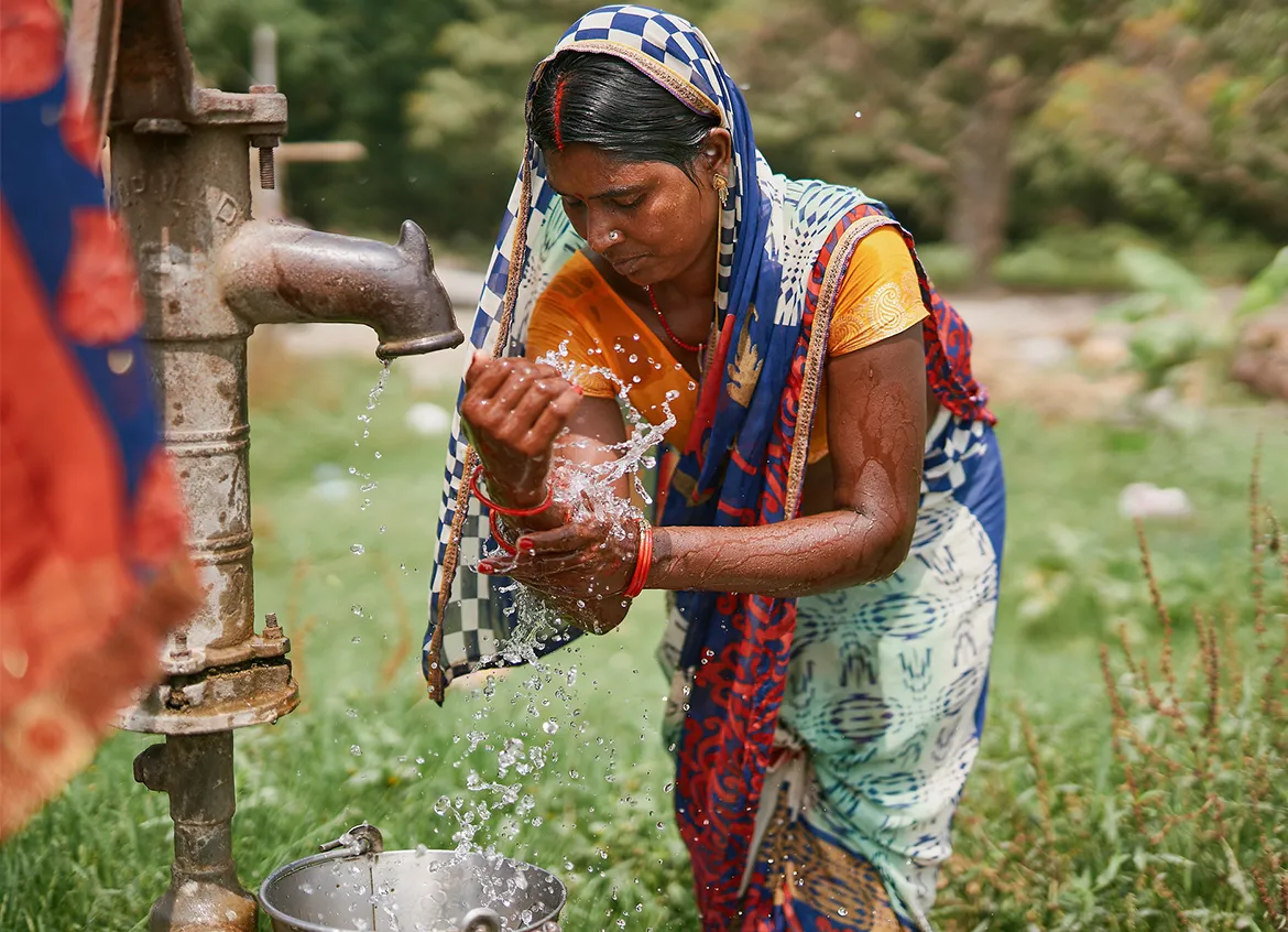 A woman in India washes her hands under a flowing water tap.