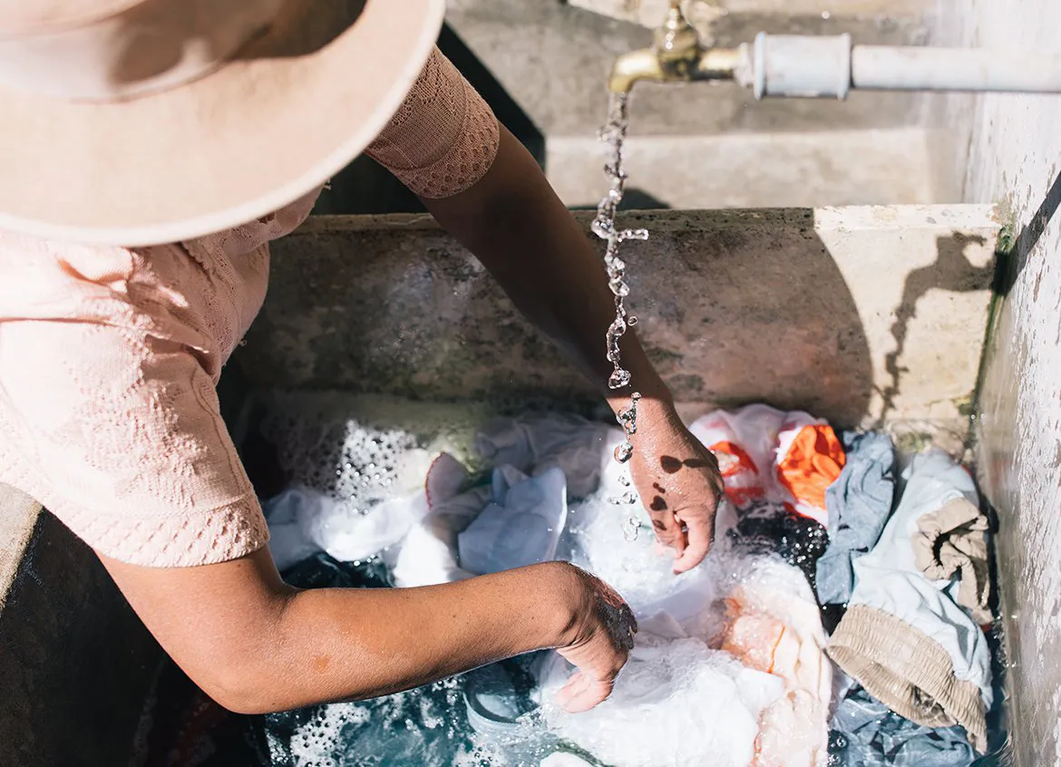 Woman washing her family's clothing in sink outside of home.