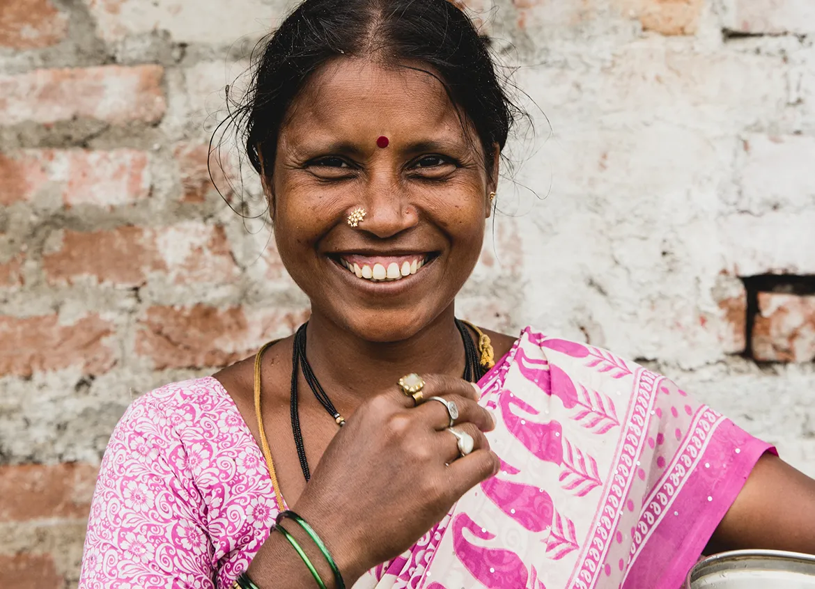 Woman wearing pink sari smiles in front of brick wall.