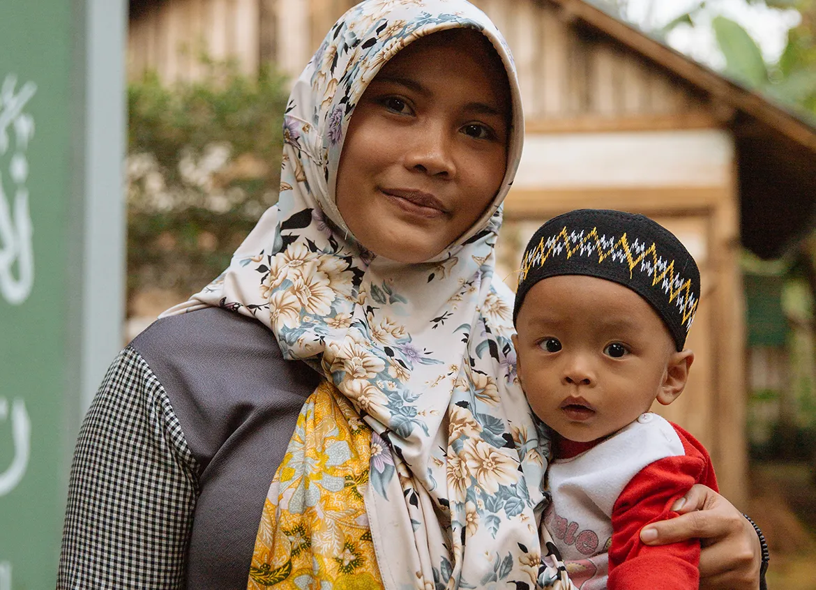 Mother holding young child in front of their home.