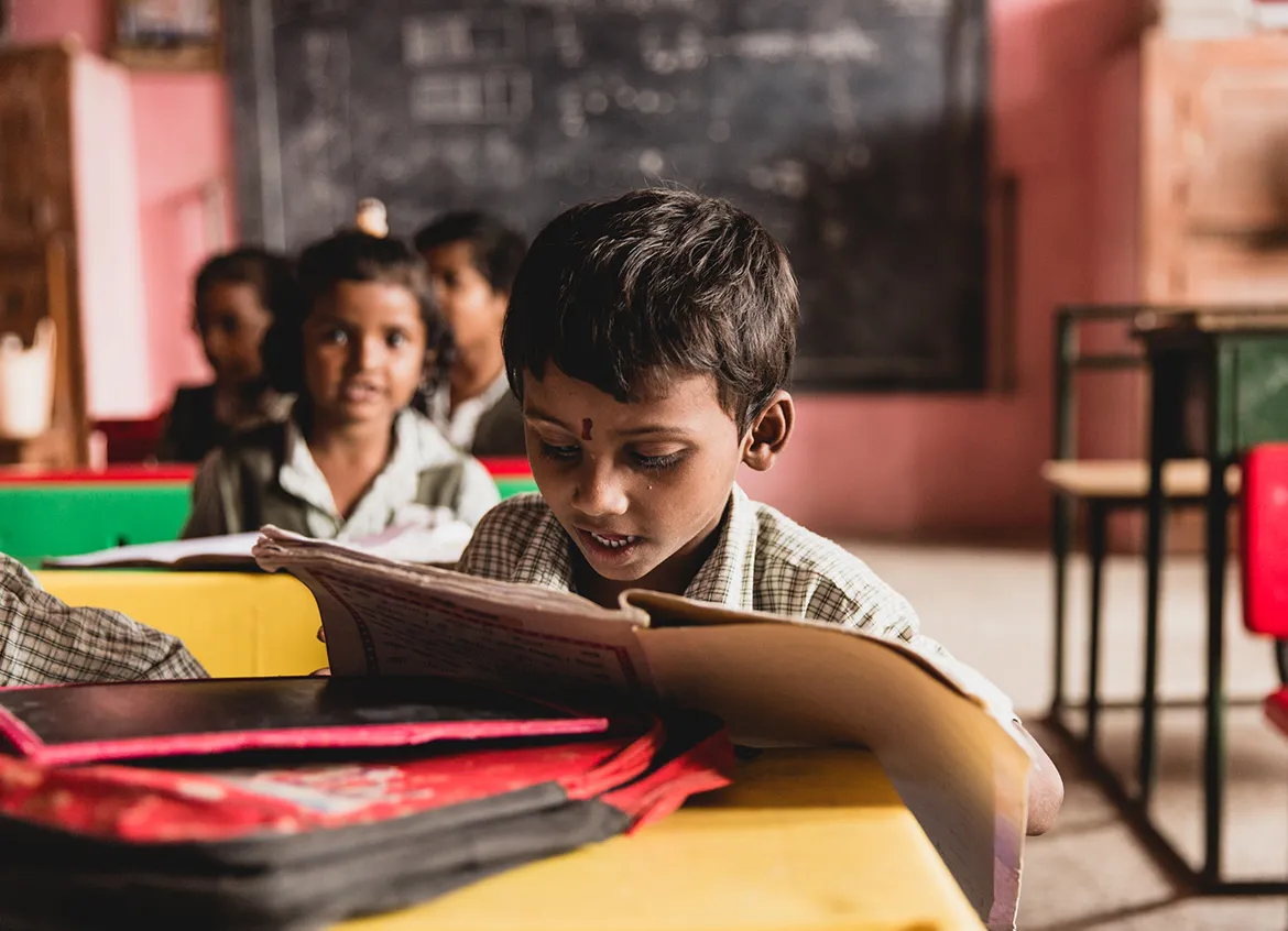 Young child reading a book in their classroom.