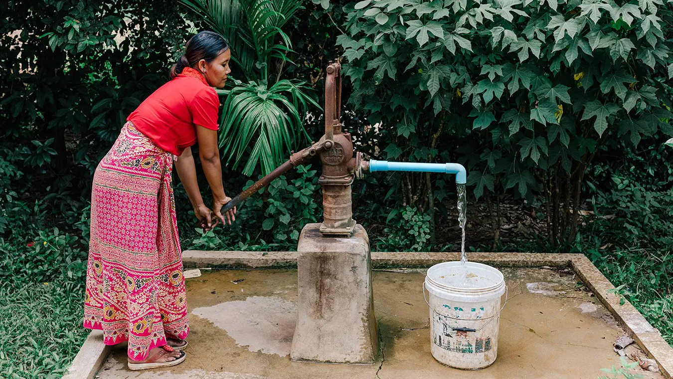 Woman at a pump filling her bucket with water.