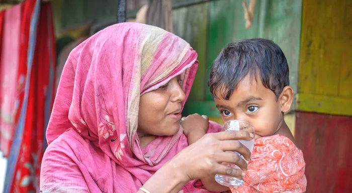 A woman in Indonesia gives her child a drink of water from a clear glass.