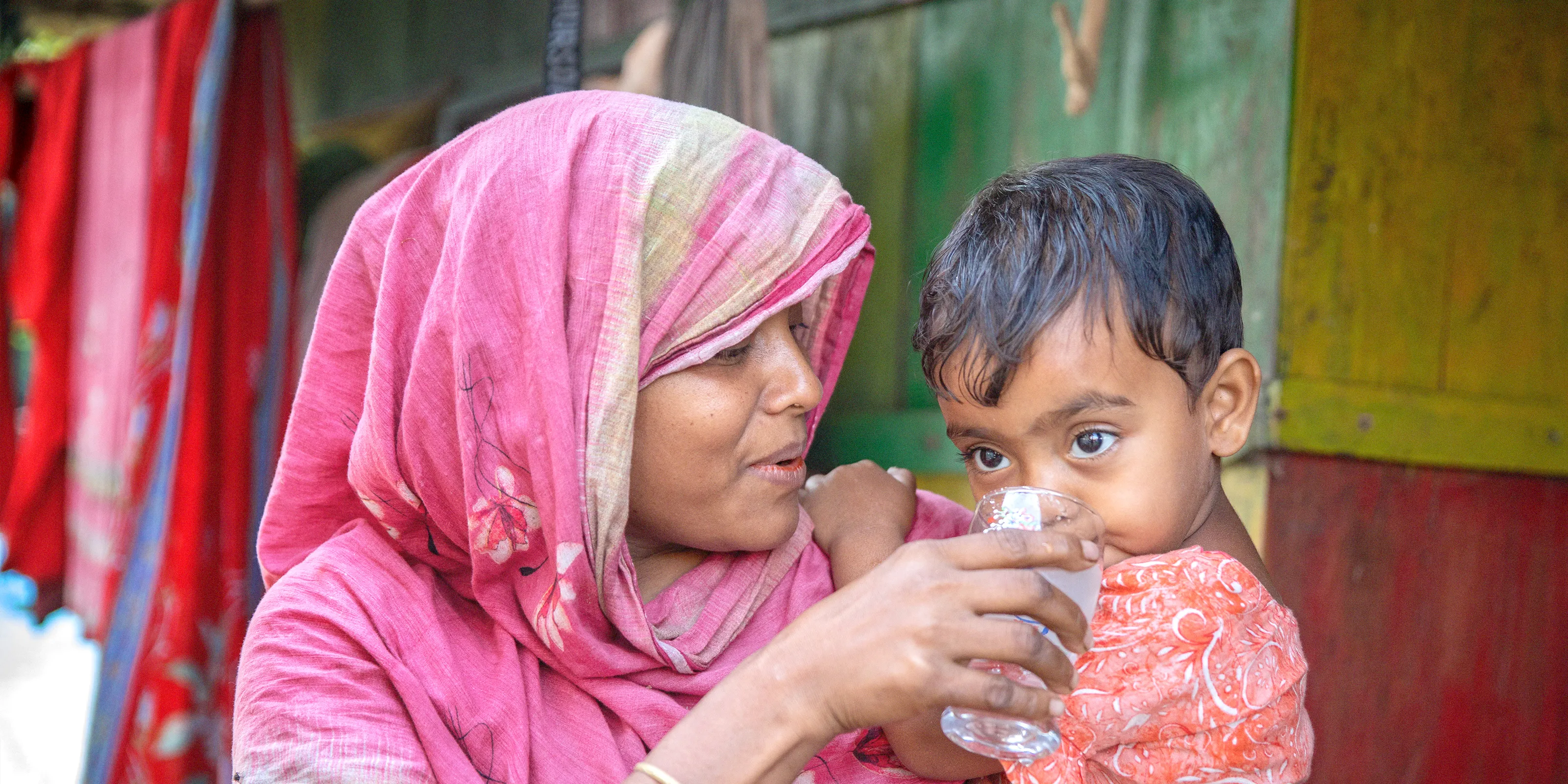 A woman in Indonesia gives her child a drink of water from a clear glass.