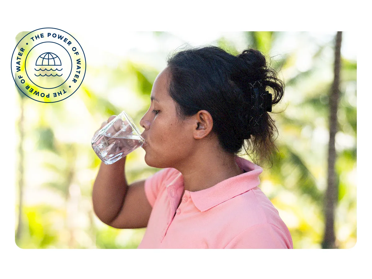 A woman in the Philippines drinks water from a clear glass.