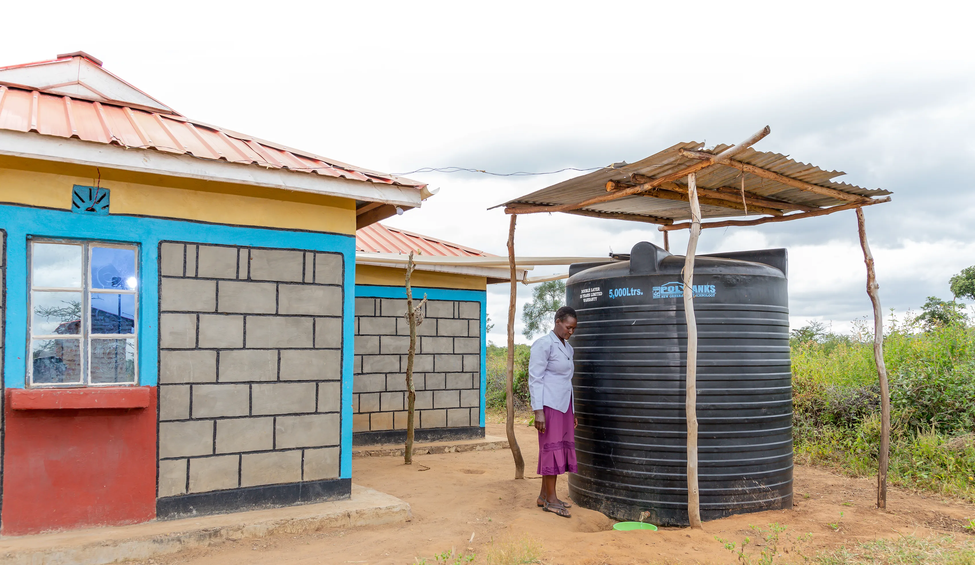 A woman in Kenya standing next to her rainwater catchment system.