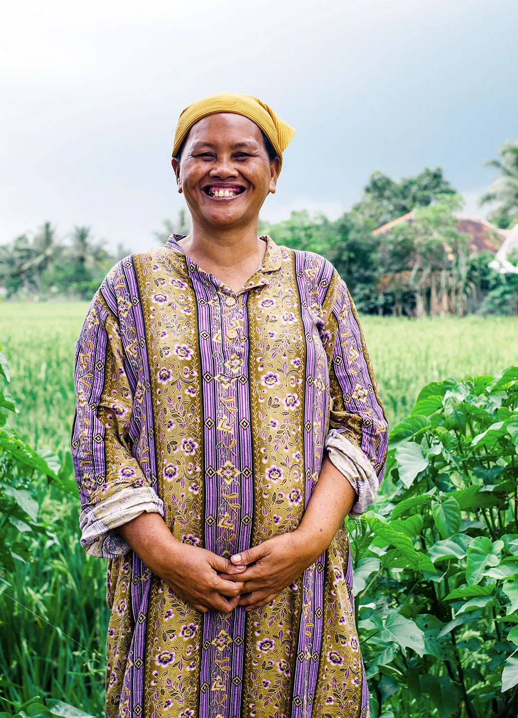 Aisyah, a woman in Indonesia smiling as she stands in a field of crops she grew.