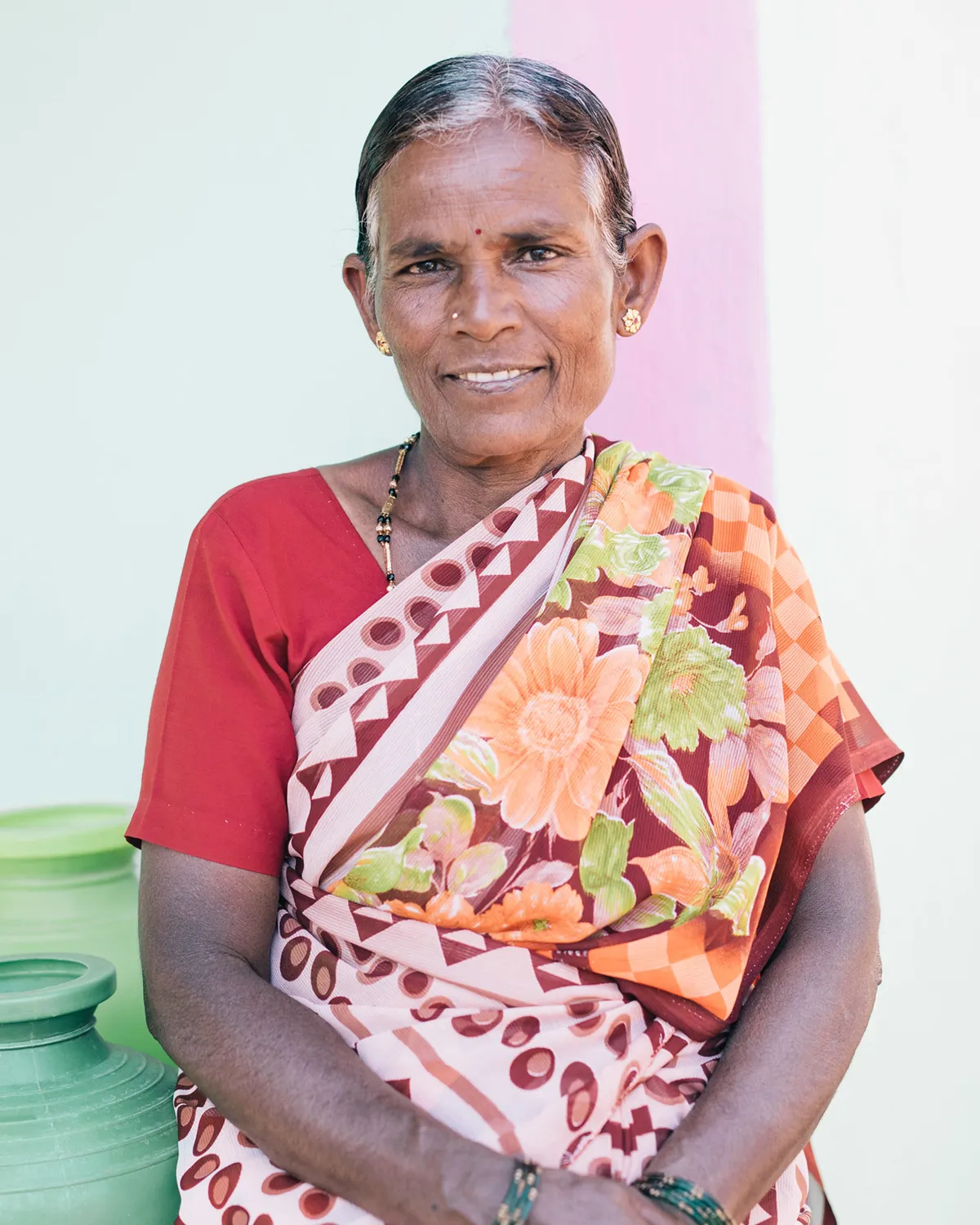 Smiling woman sitting in front of water vessels wearing a colorful sari.