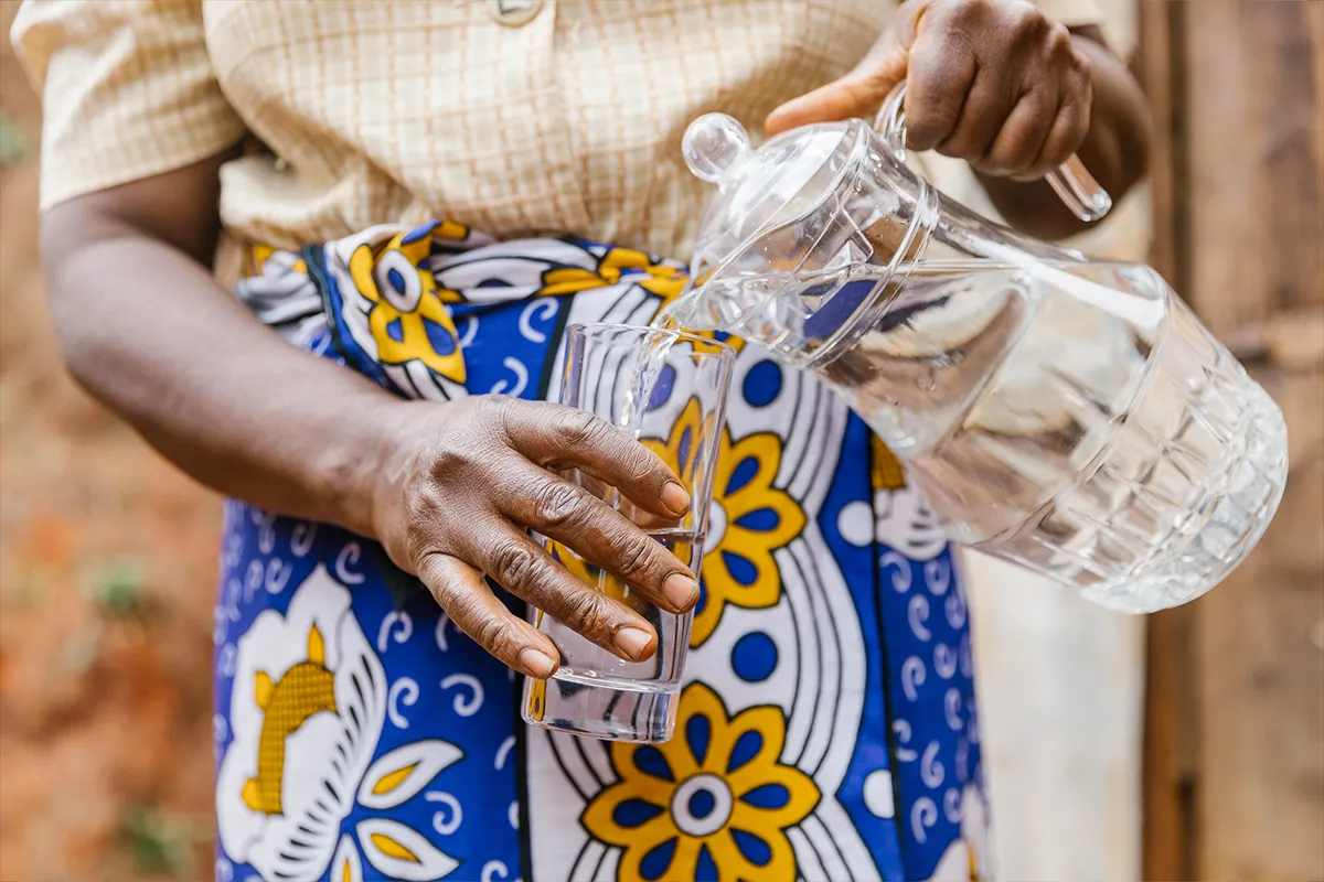 Woman pouring water from a pitcher into clear drinking glass,