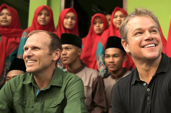 Water.org founders Gary White and Matt Damon smiling in front of a group of people.