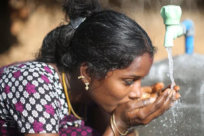 Woman drinking water from a teal water spigot.