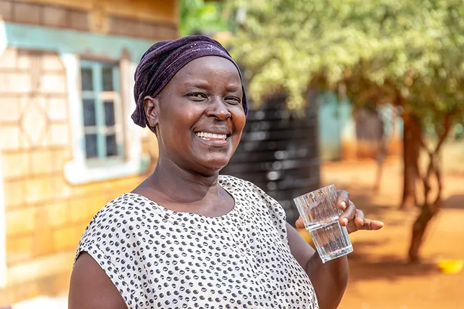 Woman smiling and holding a clear glass of water in front of her home.