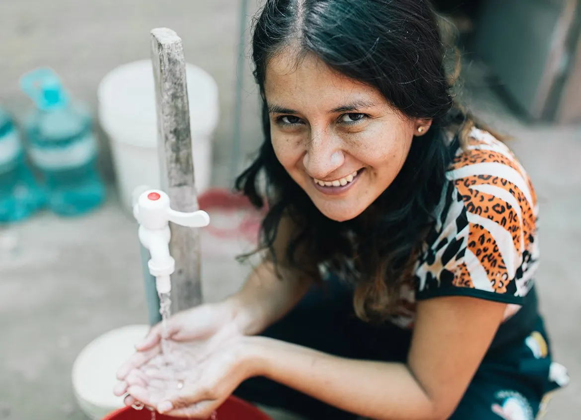 Woman smiling as she holds her hands under a safe water tap.