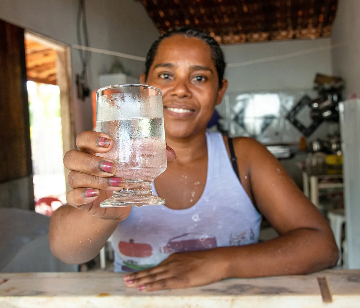 Woman named Erenice smiling while holding a clear glass of safe water at her home in Brazil.