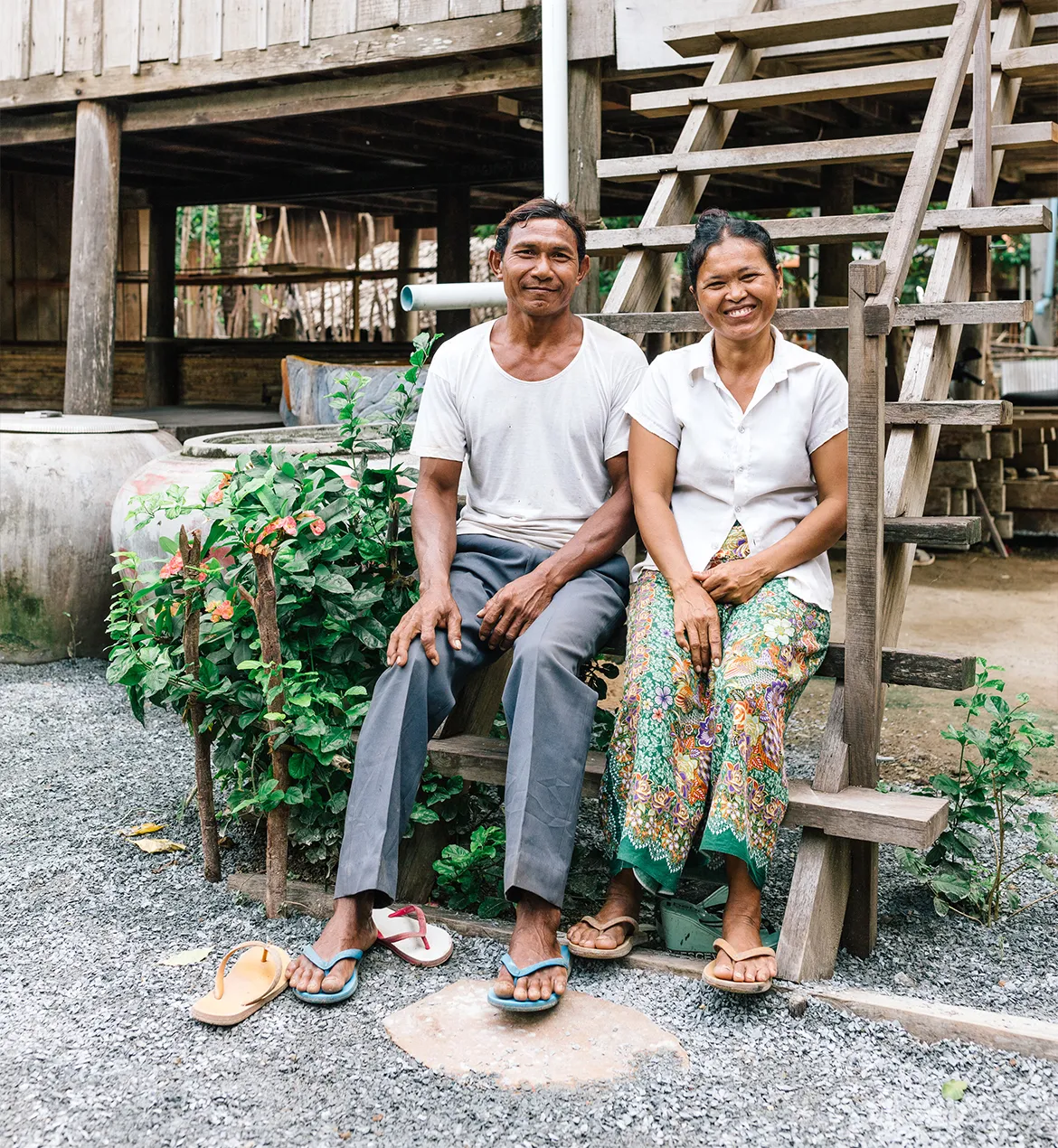 Young couple smiling while sitting on the steps outside of their home in Cambodia.