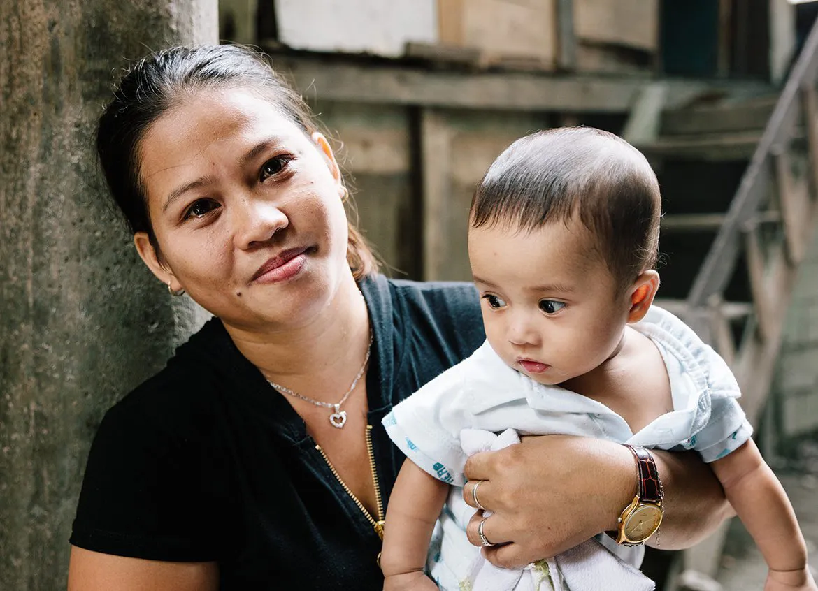 A young mother smiling and holding her baby in Cambodia.