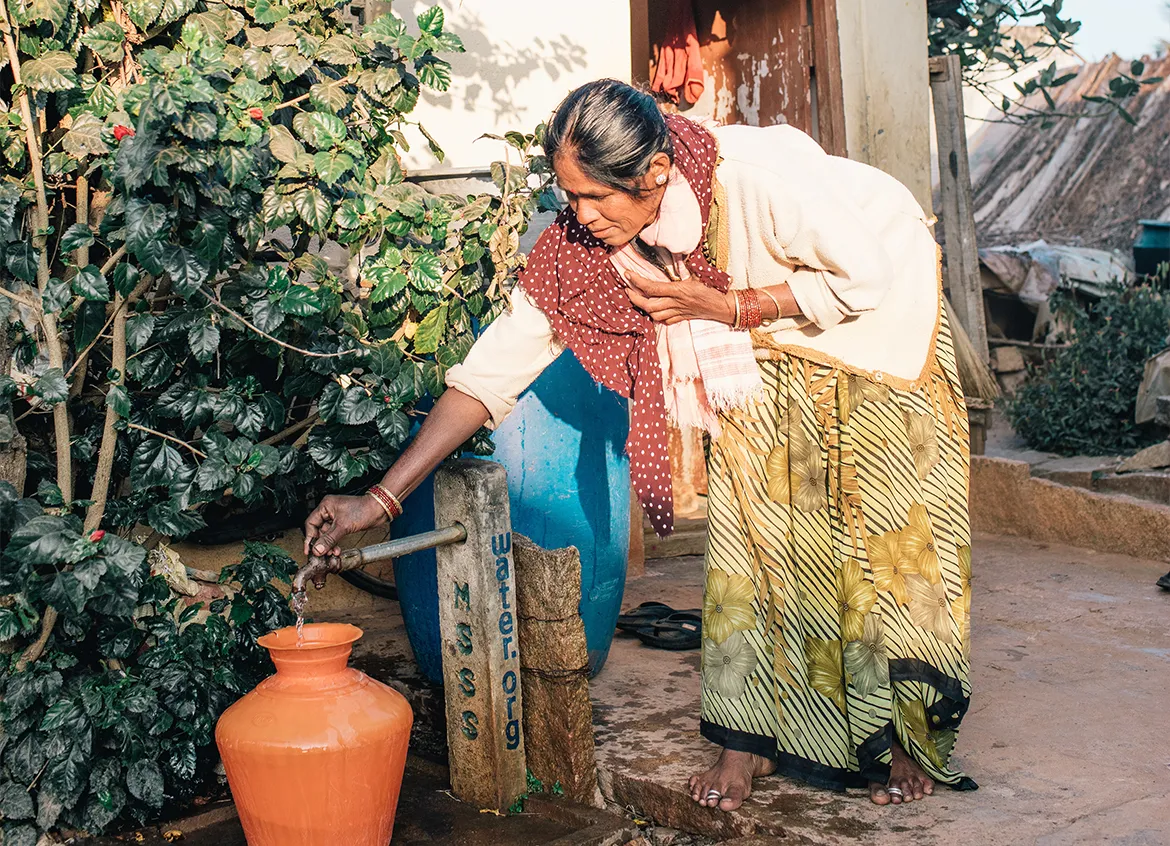 Woman filling up an orange water vessel from a tap outside her home in India.