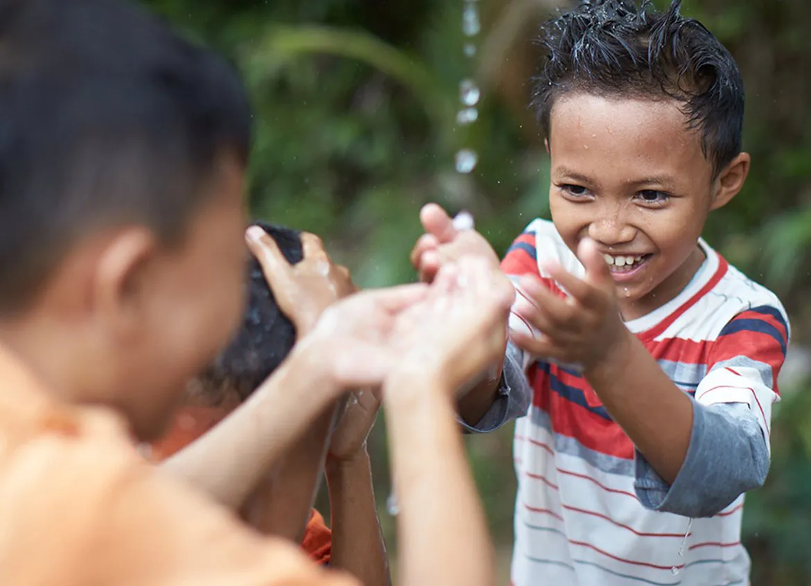 Three young children getting their hair wet while playing under a water spout.