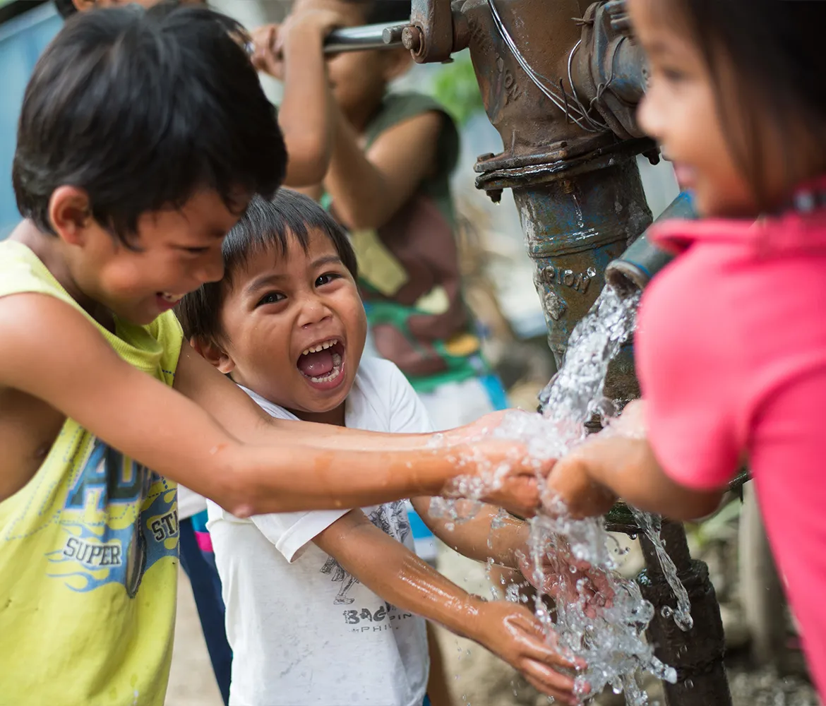 Young children playing in a water spout in the Philippines.