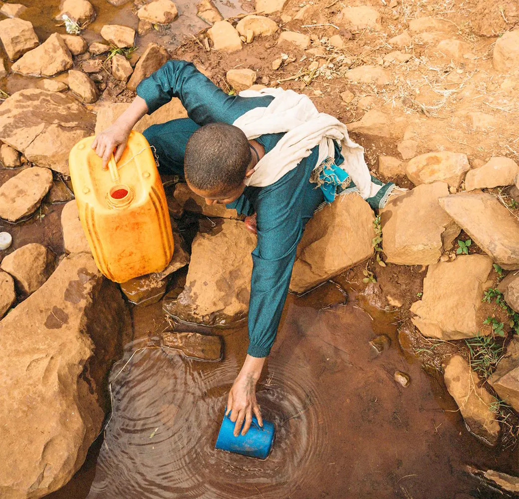 Woman collecting water from a pond, an unsafe water source.