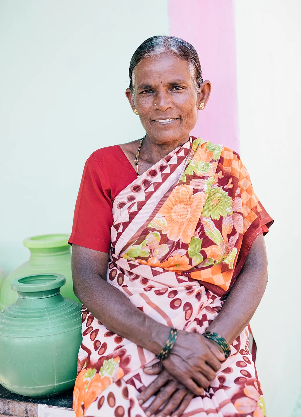 Woman smiling while she sits next to vessels of water in India.