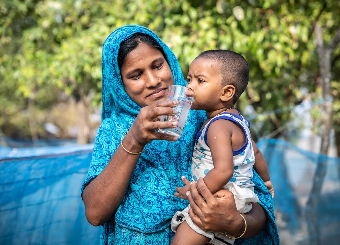 A woman in Bangladesh gives her baby a drink of water.