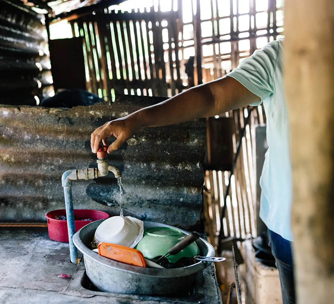 A woman washing dishes from the water tap in her home.