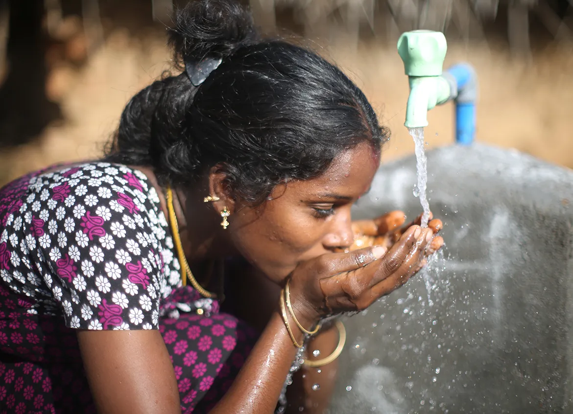 Woman drinking water from her hands under a water tap.