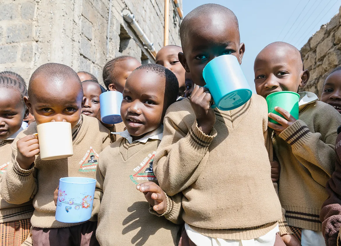 Group of young children in school uniforms drinking water out of cups outside of their school in Kenya.