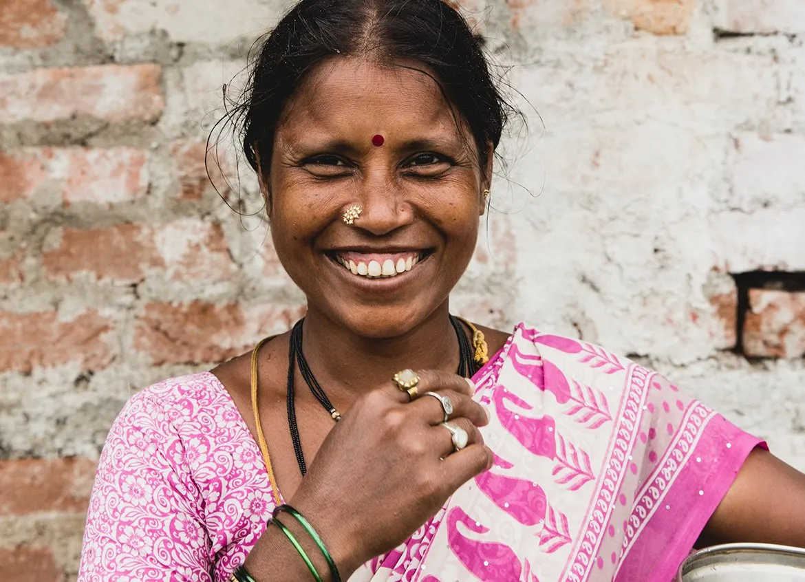 A woman smiling while holding a large silver water vessel in India.