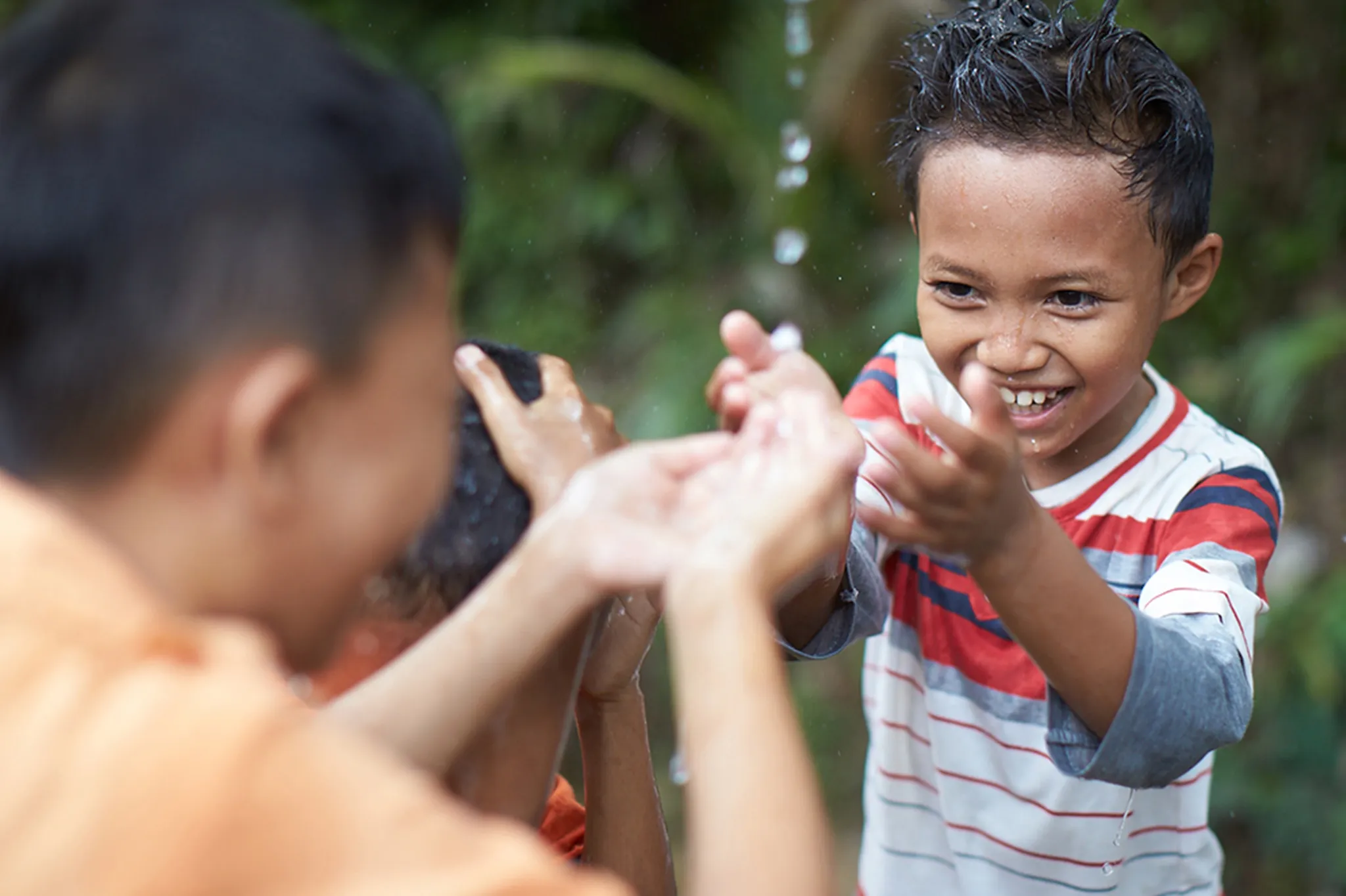 Three young children get their hair wet from a water spout.