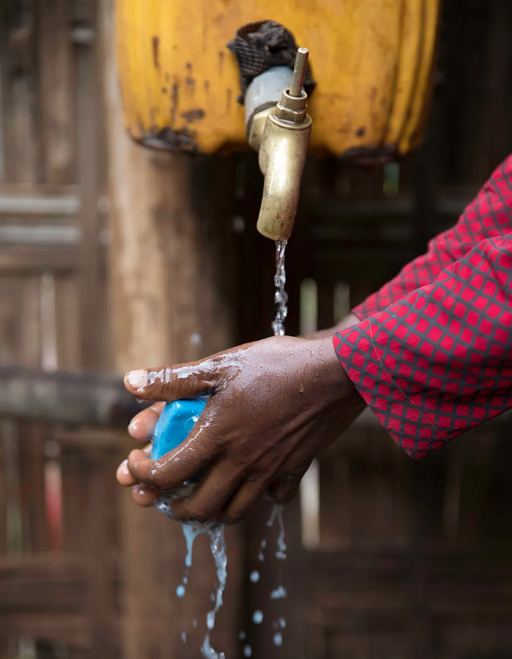 A person washing their hands under a flowing water spout using a blue bar of soap.