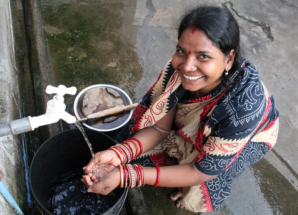 Woman in India washing her hands from a water spout.