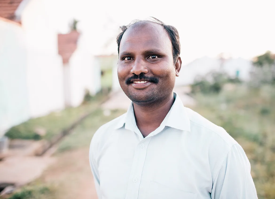 Man in a white button-down shirt smiling outside of his home.