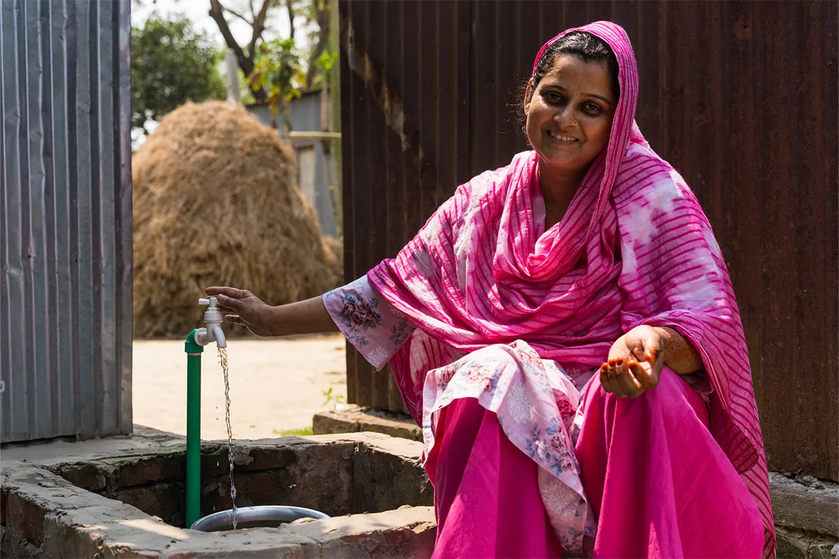 Woman in Bangladesh filling up a bucket from a water spout outside her home.