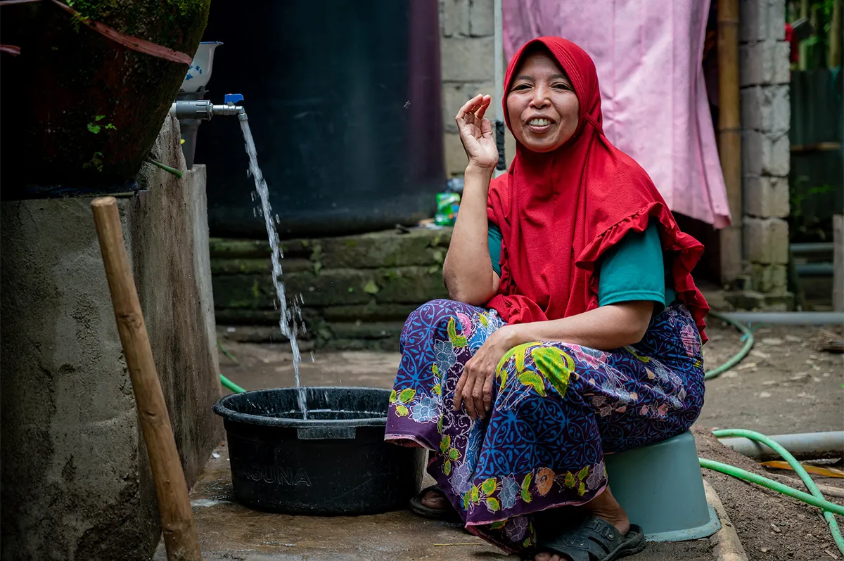 Woman in Indonesia filling up a bucket from a water spout outside her home.