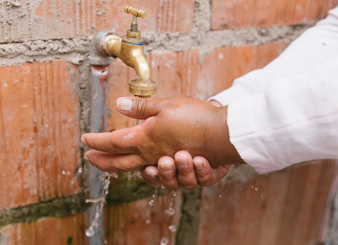 Person washing their hands using a water spout connected to a brick wall.