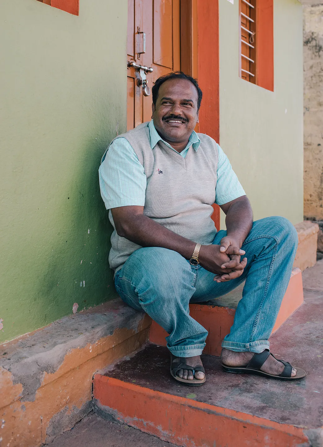 Man smiling while sitting on the stairs in front of his home.