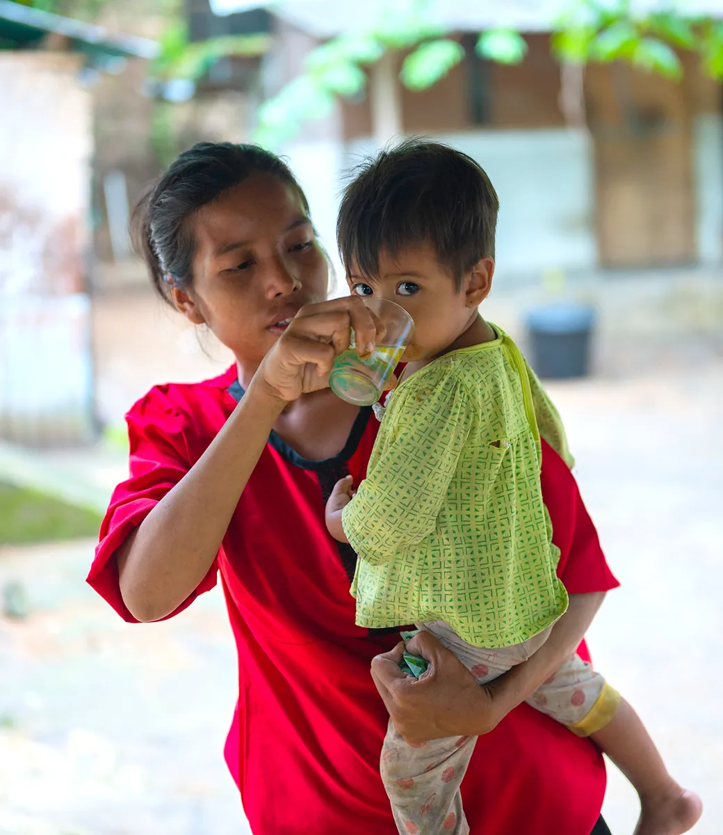 Mother holding water glass for her young child to drink from.