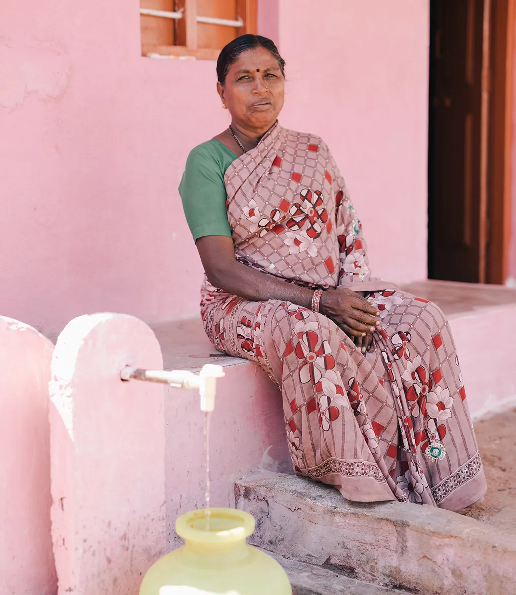 Woman filling up water vessel from a spout in front of her home.