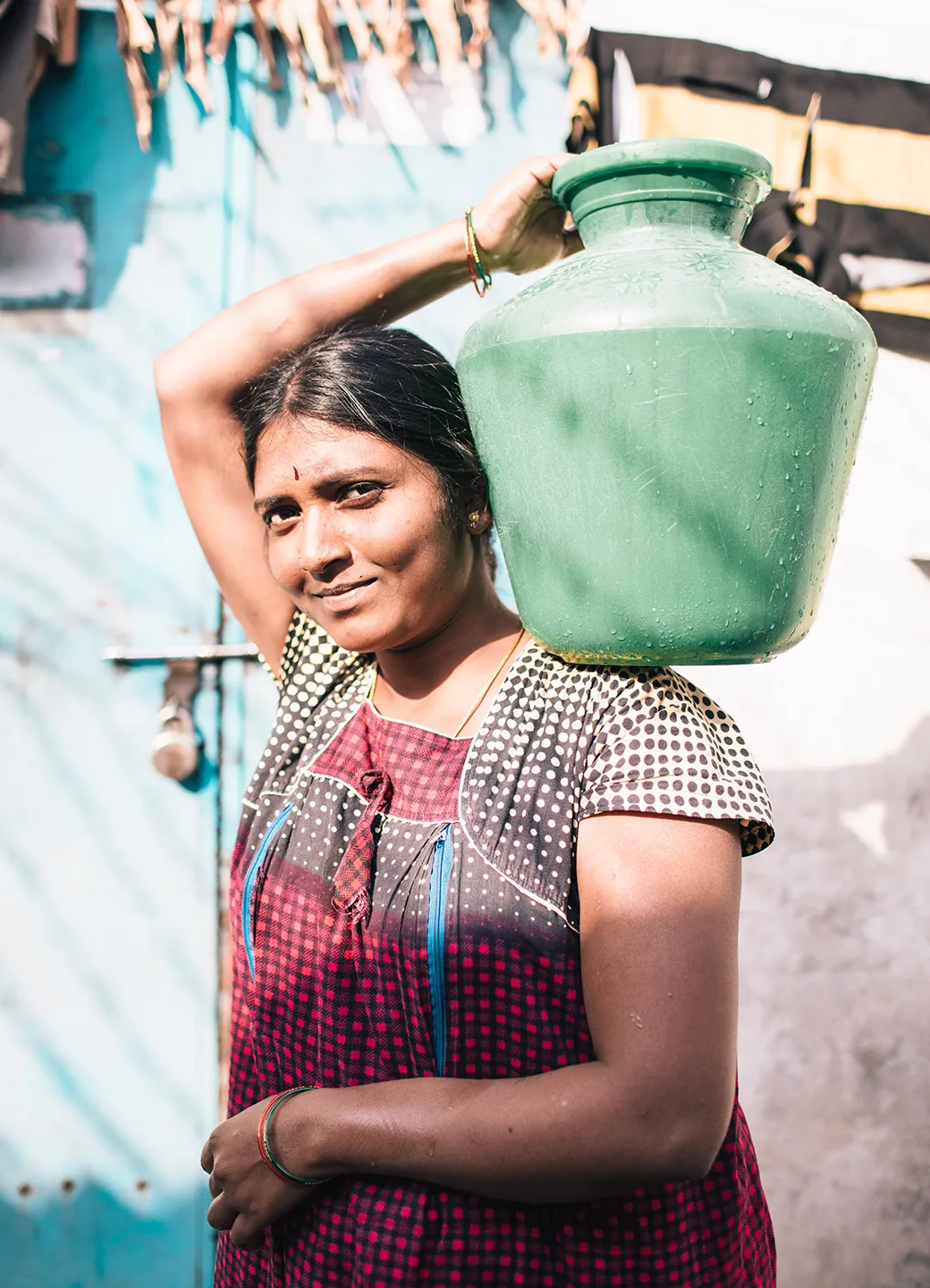 Woman carrying a teal water vessel on her left shoulder.