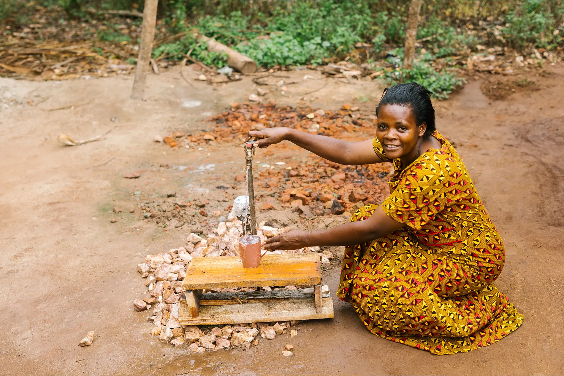 A woman named Zawelde using a water tap to fill her mug outside of her home in Uganda.